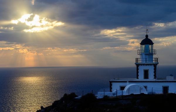Белый маяк на берегу в лучах солнца у моря 