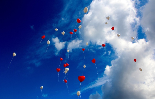 Many heart shaped balloons in the sky with white clouds