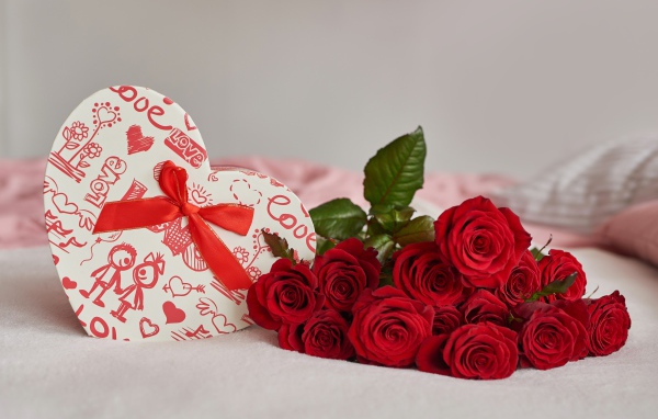 Букет красных роз с коробкой в форме сердца на кровати 