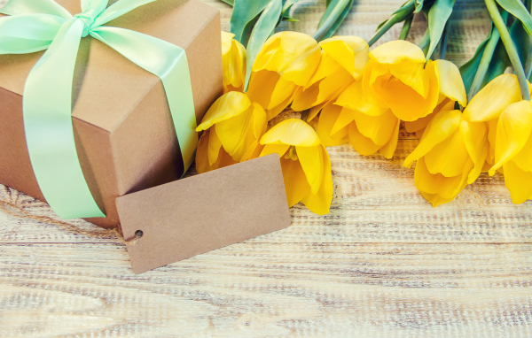 Букет желтых тюльпанов с подарком на столе 