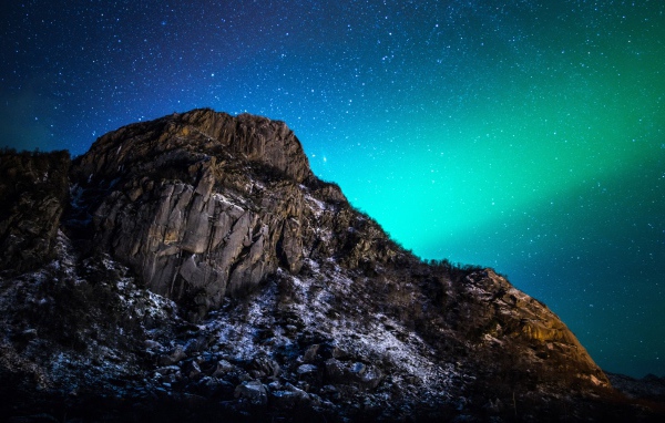 Красивое зеленое полярное сияние в звездном небе над горой 