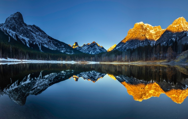 Вершины гор в лучах солнца отражаются в озере