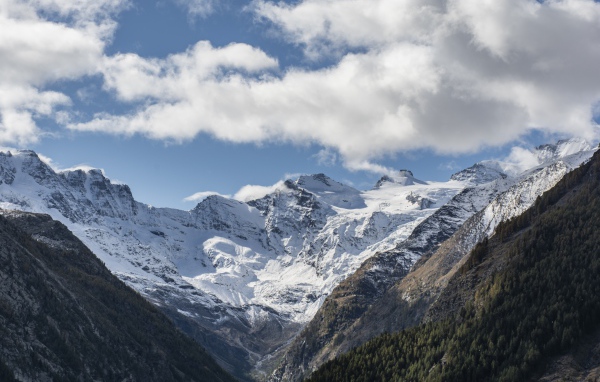Заснеженные горы под голубым небом с белыми облаками