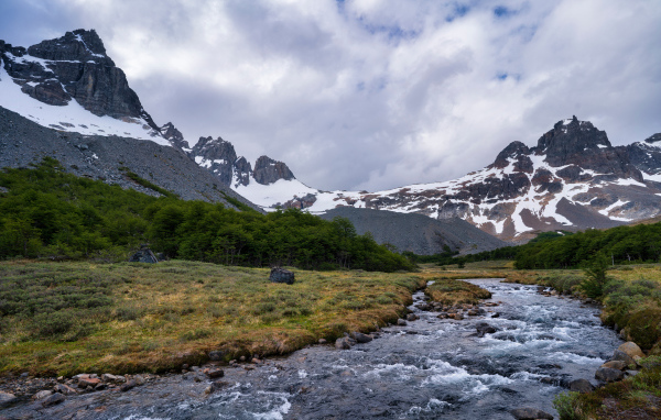 Быстрая река у заснеженных гор под густыми белыми облаками