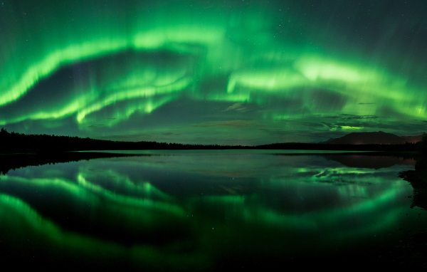 Зеленое северное сияние отражается в воде озера ночью 