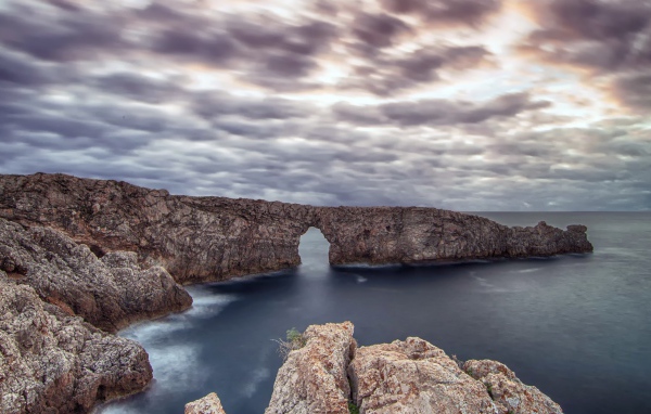 Arch in the rock in the sea under a cloudy sky