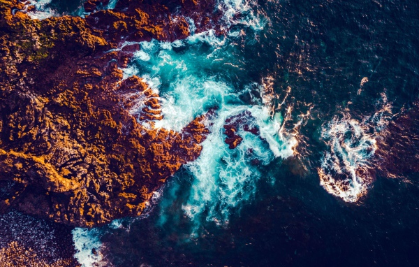 Белые морские волны бьются об камни, вид сверху