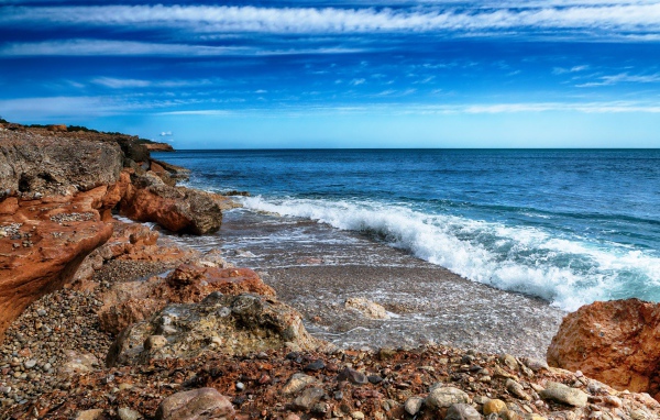 Белые волны на берегу моря с большими камнями под голубым небом