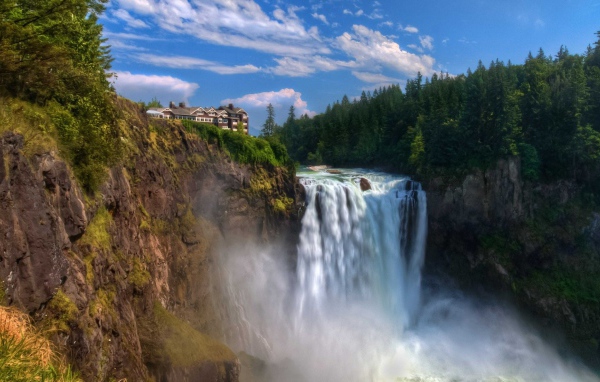 Быстрая вода водопада стекает с утеса у хвойного леса 