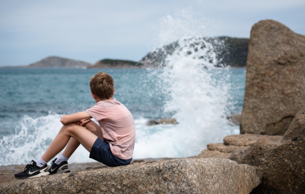 Мальчик сидит на камнях у бушующего моря