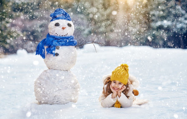 Милая девочка лежит на снегу у снеговика зимой