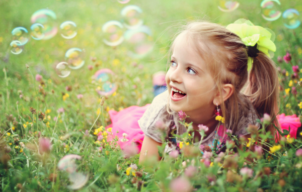 Cheerful girl lies on the grass with soap bubbles