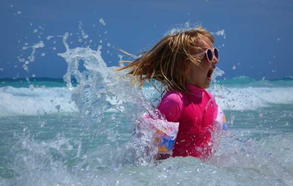 Веселая маленькая девочка купается в море летом