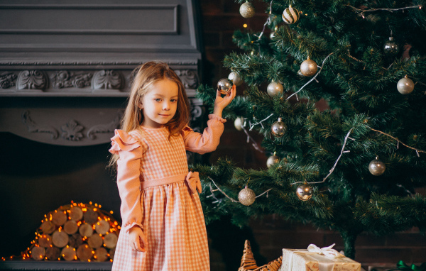 Милая маленькая девочка стоит у наряженной елки 
