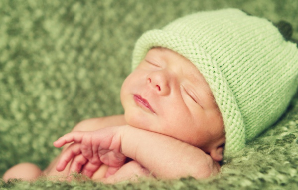 Зеленая вязаная шапка на голове у спящего ребенка 