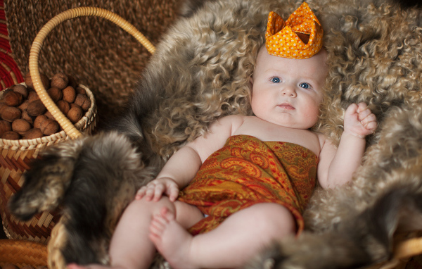 Маленький грудной ребенок в короне лежит в корзине 