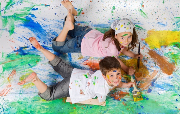 Маленькие мальчик и девочка рисуют красками на полу 