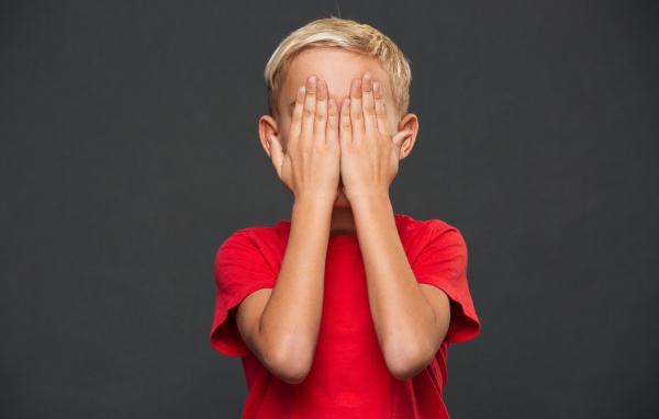 Маленький мальчик в красной футболке закрыл лицо руками 