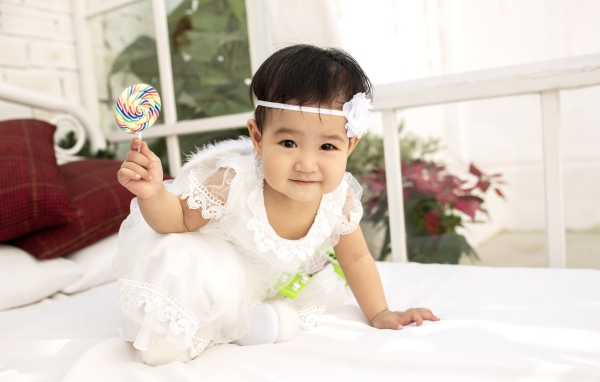 Маленькая девочка в белом платье с леденцом в руке