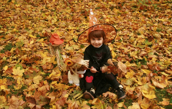 Маленькая девочка в костюме ведьмы сидит на опавшей листве на Хэллоуин