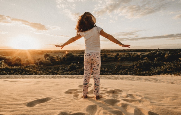 Маленькая девочка стоит на песку в лучах солнца