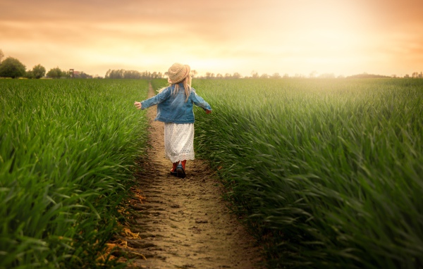 Маленькая девочка идет по полю с зеленой травой 