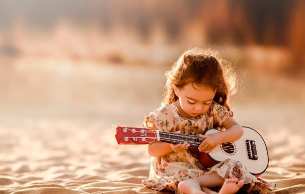 Маленькая девочка с гитарой сидит на песке 