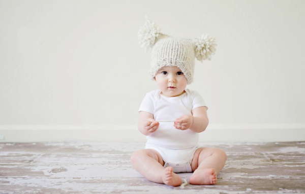 Маленький грудной ребенок в боди с шапкой на голове