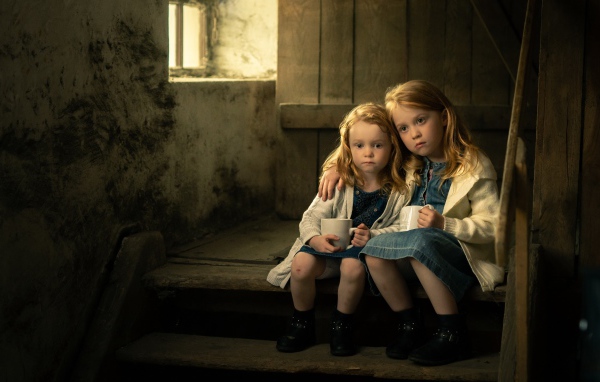 Две маленькие сестры пьют какао на ступеньках дома