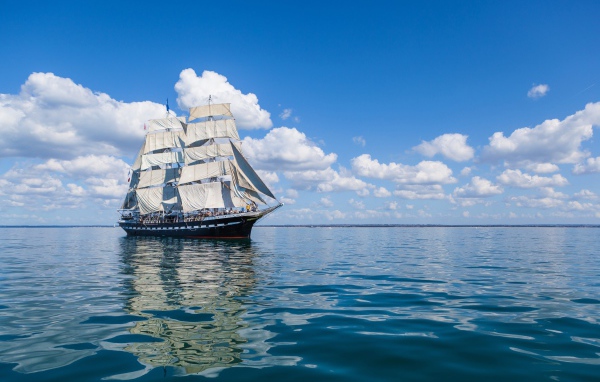 Большой корабль с белыми парусами в море под голубым небом