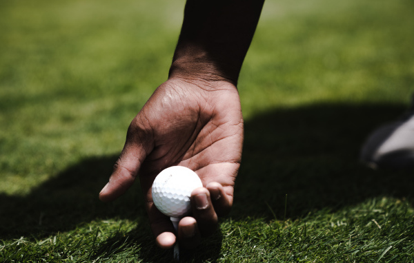 Белый мячик для гольфа в руке у мужчины на поле 