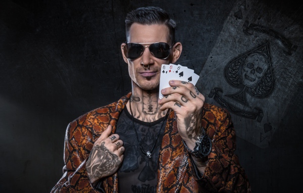 Мужчина с татуировками на теле держит в руке три карты шестерки 