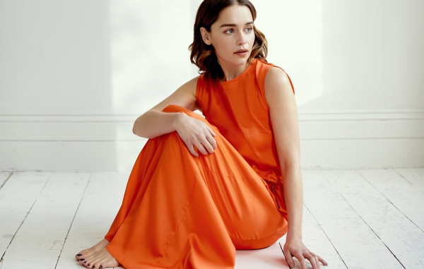 Актриса Эмилия Кларк  в оранжевом платье сидит на полу