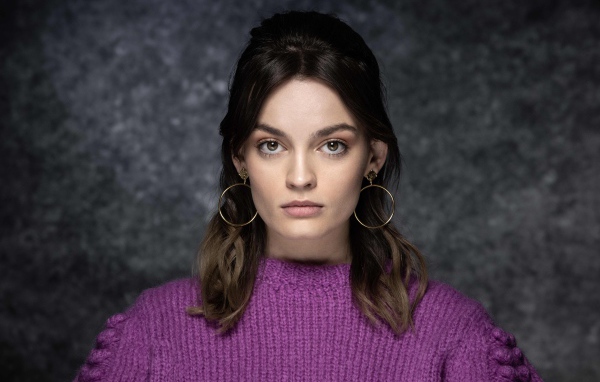 Актриса Эмма Маккей в сиреневом свитере на сером фоне