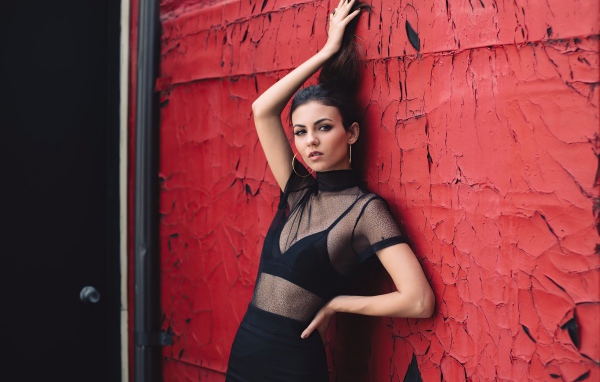 Актриса Виктория Джастис в черном наряде на фоне красной стены