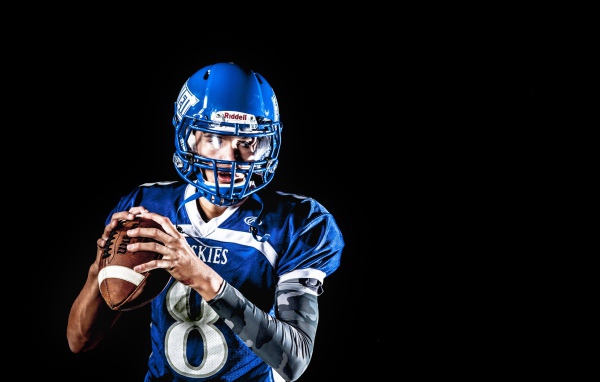 Игрок в американский футбол с мячом в руках на черном фоне 