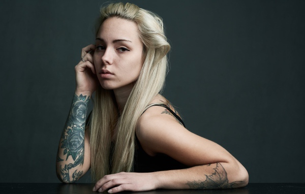 Красивая блондинка с татуировками на теле на сером фоне