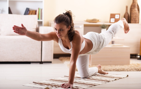 Красивая девушка в белом костюме занимается фитнесом дома