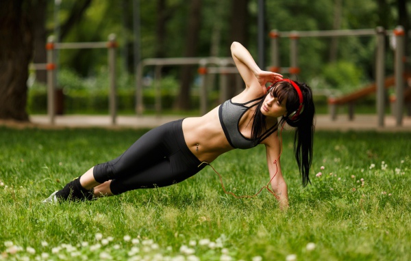 Девушка с наушниками на голове занимается фитнесом на траве 