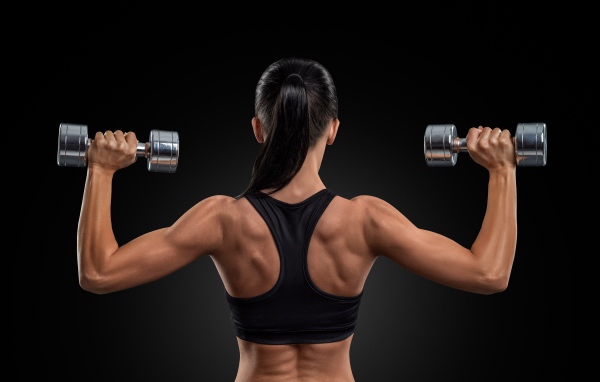 Стройная спортивная девушка с гантелями в руках на черном фоне