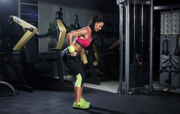 Девушка занимается с гантелями в спортзале у тренажеров 