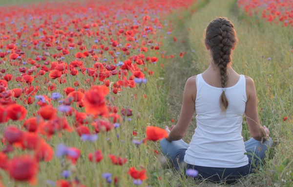 Молодая девушка медитирует на поле с красными маками
