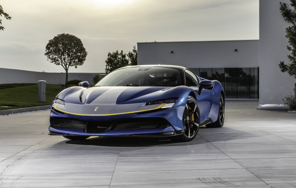 Голубой спортивный автомобиль Ferrari SF90 Stradale Assetto Fiorano 2021 года у здания