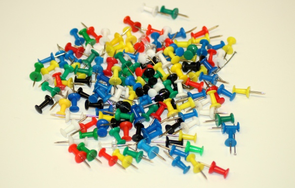 Разноцветные канцелярские гвозди на белом фоне