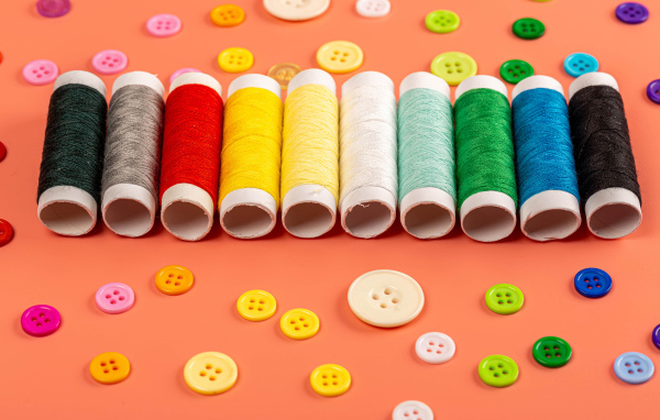 Разноцветные нитки и пуговицы на розовом фоне