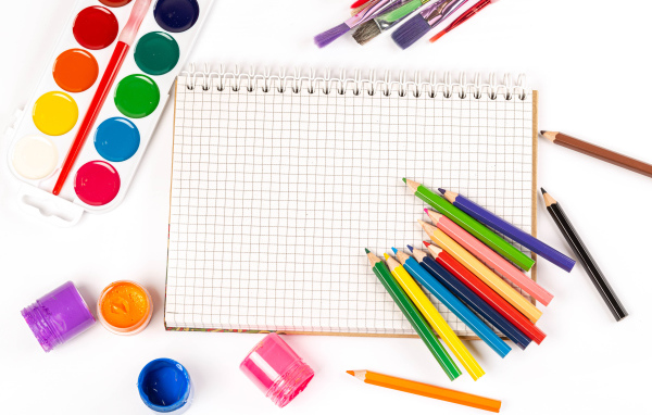 Карандаши, краски и тетрадь на белом фоне 