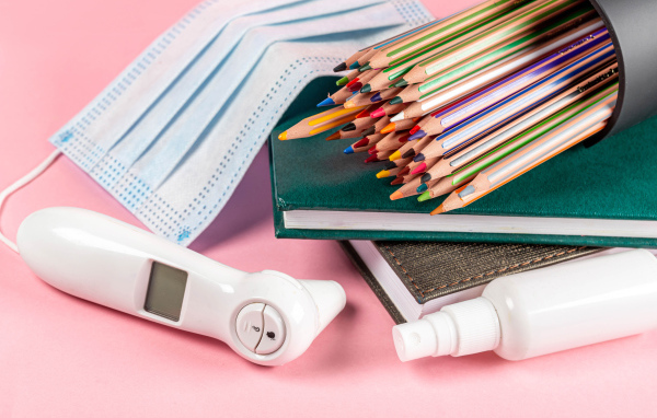 Карандаши, градусник, маска и блокнот на розовом фоне 