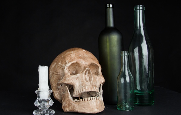 Череп, пустые бутылки и свеча на черном фоне