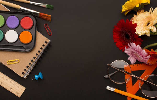 Канцелярские предметы, очки и герберы на черном фоне 