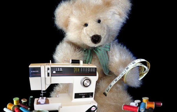 Игрушечный медвежонок со швейной машинкой на черном фоне 